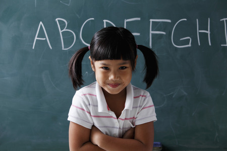 young girl with pony tails smiling in front of chalk boardの写真素材
