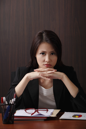 Woman sitting at desk with head on hands frowningの写真素材