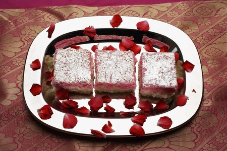 Indian pink sweets on silver tray with rose petals.の写真素材