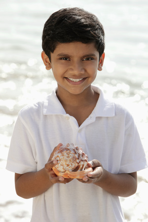 Young boy holding sea shell and smilingの写真素材