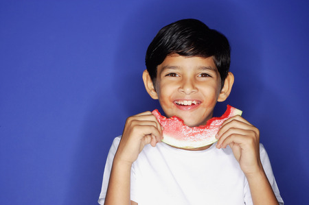 Boy looking at camera, holding half eaten slice of watermelonの写真素材