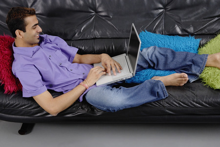 Man lying on sofa using laptopの写真素材