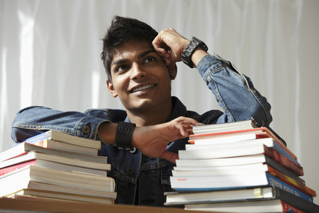 young man with a stack of books smiling and thinkingの写真素材