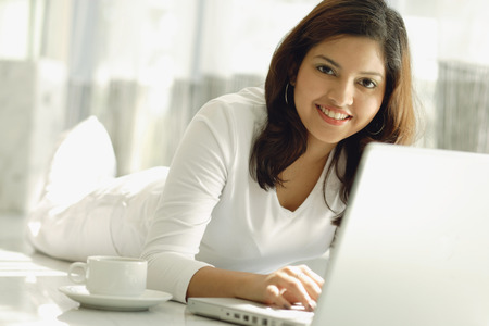 Woman at home with laptop, smiling at cameraの写真素材