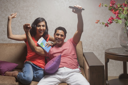 India, Man and woman watching television with arms raisedの写真素材