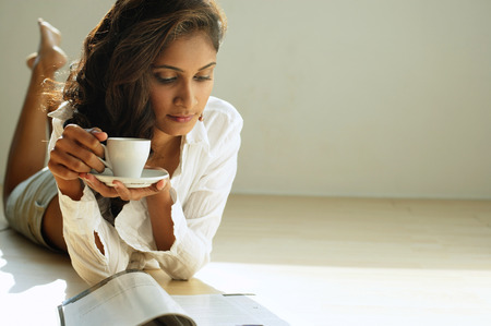 Woman looking at magazine, holding cup and saucerの写真素材