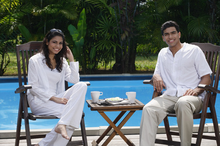 Couple sitting by the pool, looking at cameraの写真素材