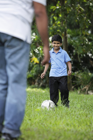 Young boy kicking ball to his fatherの写真素材