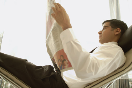 Businessman reclining on chair, reading newspaperの写真素材