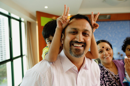 Family of four smiling at camera, father carrying son on backの写真素材