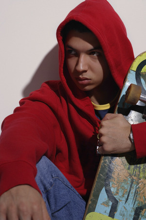 young man wearing red hooded sweatshirt holding skateboardの写真素材