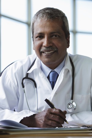 Indian doctor sitting at desk and smilingの写真素材