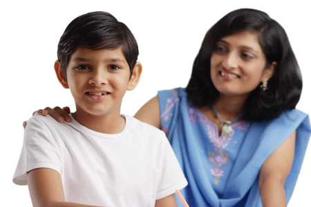 Boy looking at camera, mother behind him with her hand on his shoulderの写真素材