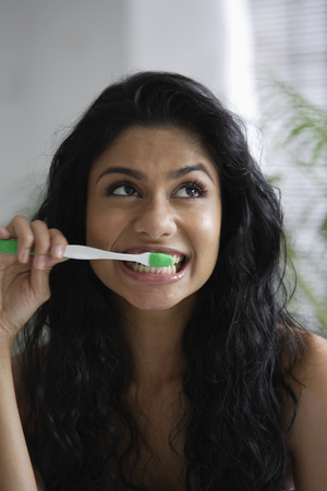 Head shot of Indian woman brushing her teeth and looking upの写真素材