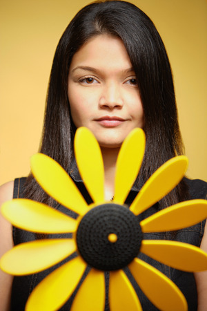 Young woman against yellow background, pin wheel in front of herの写真素材