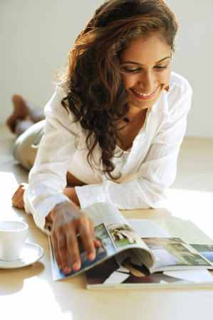 Woman lying on front, looking at magazine, smilingの写真素材