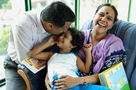 Family with one child, father kissing daughter's head, mother smiling at cameraの写真素材