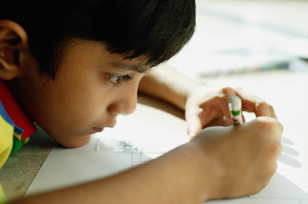 Boy with chin on floor, drawing with crayonsの写真素材
