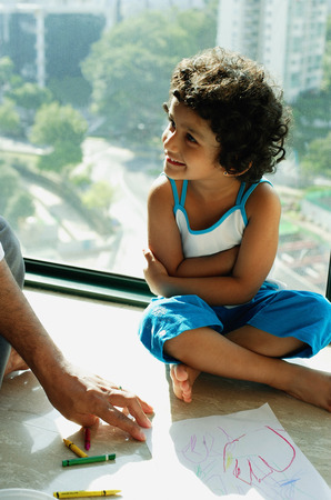 Girl sitting on floor looking away, fathers hands in foregroundの写真素材