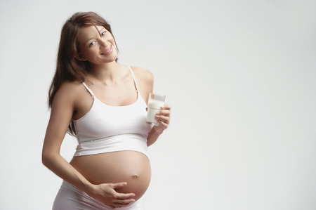 Pregnant woman standing, glass of milk in handの写真素材