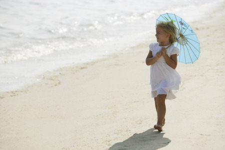 little girl walking on beach under blue umbrellaの写真素材