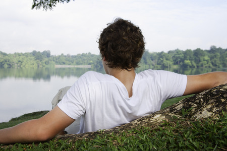 Teen boy on grass looking at lakeの写真素材