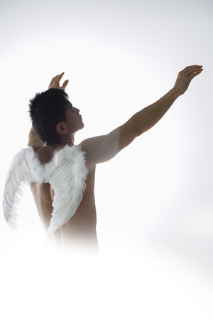 Man wearing angel wings, holding arms upwardの写真素材