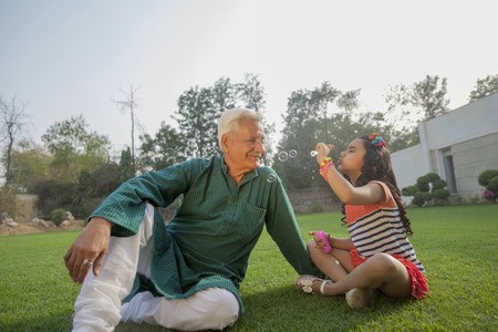 India, Young girl (6-7) blowing bubbles with grandfather sitting on backyardの写真素材