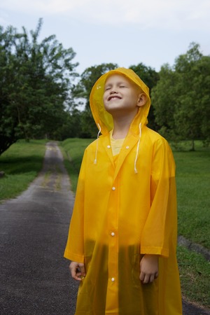 young boy standing on road in rain coatの写真素材