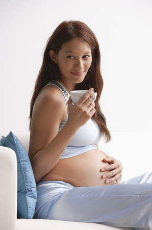 Pregnant woman, holding cup, hand on stomachの写真素材