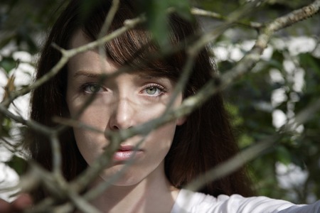 young woman looking through branchesの写真素材