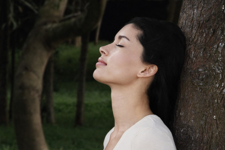 Young woman leaning against tree trunkの写真素材