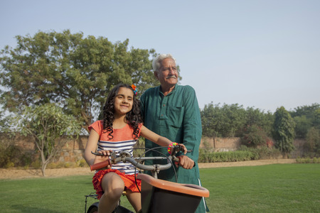 India, Grandfather teaching young girl (6-7) to ride bicycle on backyardの写真素材