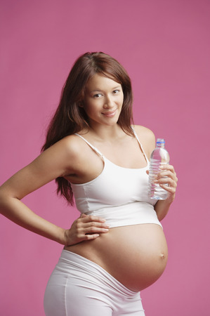 Pregnant woman standing, bottle of water in handの写真素材