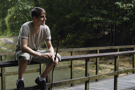 Young man sitting on railing of wooden foot bridgeの写真素材