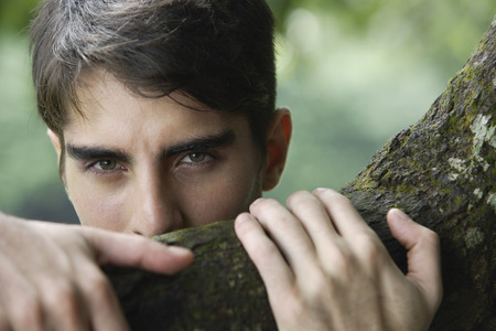 Young man peering over tree branchの写真素材