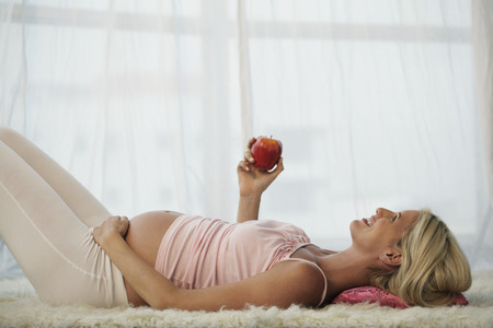 pregnant woman laying on back holding appleの写真素材
