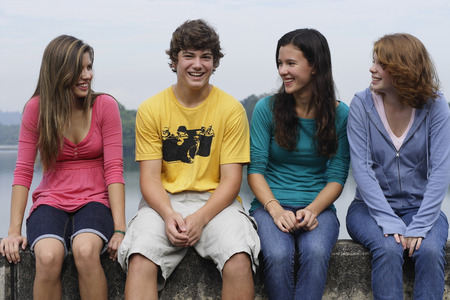 Group of teens sitting on wall next to lakeの写真素材