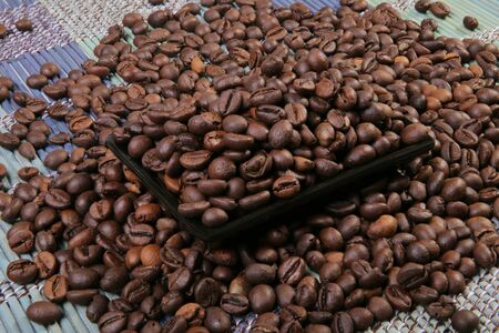 A scattering of coffee beans on a plate. Black rectangular plate. Bamboo mat.の写真素材