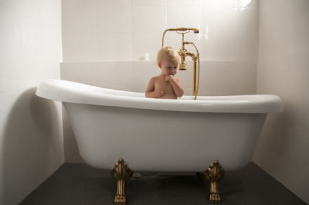 baby sitting an a bathtub with golden tapの写真素材
