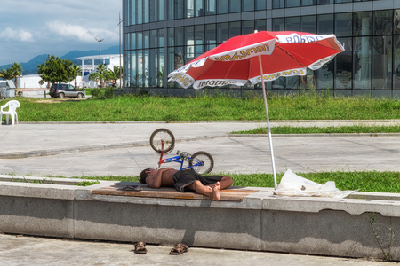 Batumi. Georgia - September 2, 2014. A boy sleepeng on a street bench under ubrella.のeditorial素材