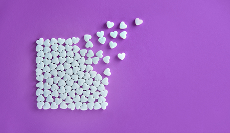 Square made of white sugar candies on a purple paper background with hearts fly awayの写真素材