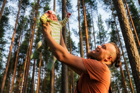 Happy bearded father holding his 3 months old sleepy baby boy on his outstretched arms.の写真素材