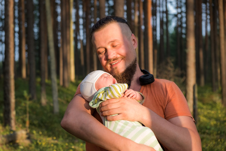 Happy father is looking at his cute little sleeping son with love and tender while holding him...