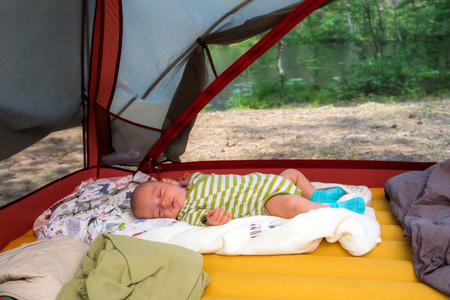 Cute baby boy tourist is sleeping in a tent in summer time outdoorsの写真素材