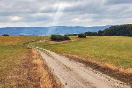 Rural ladscape with road going through a field and ray of light on a cloudy skyの写真素材