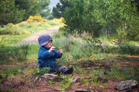 Little baby boy 1 year old sitting on a ground in a grass while trekkingの写真素材