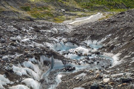 Mountain landscape with stream in ice of a glacier and green mountains around it. Source of river Adishchala.の写真素材