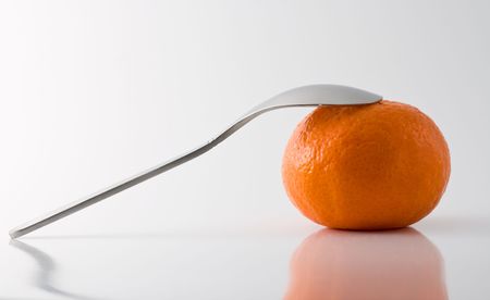 Metal teaspoon leaning on a tangerine, grey background, reflective surfaceの写真素材