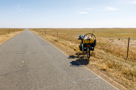 Xilin Gol, Inner Mongolia, China - September 25, 2018: a traveler's bike with bags and a spare wheel is standing on an empty asphalt road in the steppe.のeditorial素材
